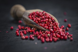 Portion of Pink Peppercorns on a rustic slate slab, selective focus, close-up shot