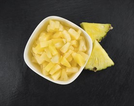 Portion of Preserved Pineapple (chopped) as detailed close up shot on a slate slab, selective focus