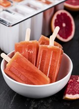 Some homemade Grapefruit Popsicles (with some fresh fruits) as close-up shot (selective focus)