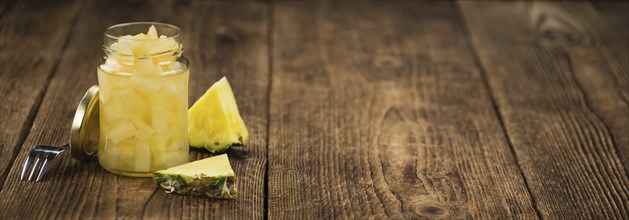 Chopped Pineapple (preserved) as high detailed close-up shot on a vintage wooden table, selective