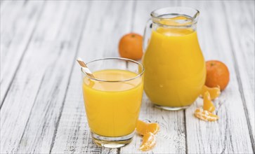 Wooden table with fresh homemade Tangerine Juice (close-up shot, selective focus)