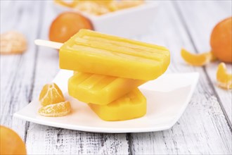 Old wooden table with a portion of homemade Tangerine Popsicles (selective focus, close-up shot)