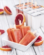 Old wooden table with freshly made Grapefruit Popsicles (selective focus, close-up shot)