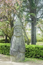 A large stone statue in a garden area with trees and bushes, in Suncheon, South Korea, Asia