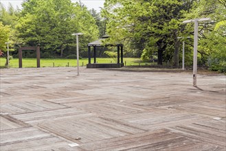 Spacious wooden deck area with scattered lamps and a pavilion, surrounded by lush green trees, in