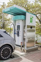 Electric vehicle charging station with a car connected, under a canopy surrounded by greenery, in