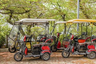 Electric golf carts parked among lush trees with a protective cover under a sunny sky, in Suncheon,