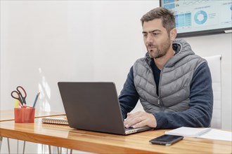 An attractive mature man with a shaved beard sits at his desk, deeply focused on his work while