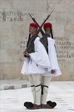 Two Evzones in traditional dress shoulder to shoulder, standing guard in front of the Parliament