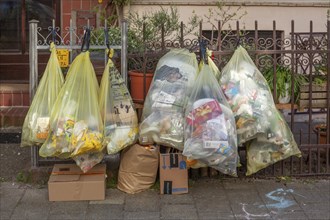 Yellow bags for plastic waste, hanging on a garden fence in front of a house entrance, waste