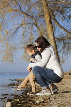 A woman and a child are kneeling by a lakeshore in autumn, enjoying the nature and calm atmosphere,