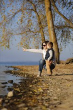 A woman and a child enjoy a moment by the lakeshore on an autumn day, with falling leaves adding to