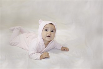 Baby in pink costume with ears hood, laying on a white background looking up