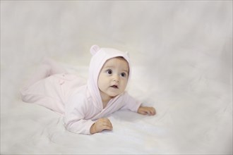 A baby in a pink onesie with ears lies on a soft white surface