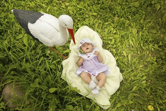 A baby lies on a blanket on grass next to a stork statue on a sunny day, Belarus.Minsk