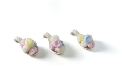 Cotton balls of different colors on white ceramic spoons on a white background