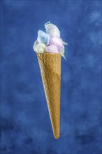 Different colored cotton balls in an ice cream cone on a blue background