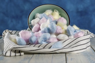 Cotton balls of different colors in a ceramic bowl on a blue background