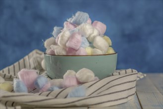 Cotton balls of different colors in a ceramic bowl on a blue background