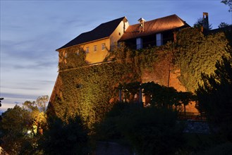 An illuminated castle at dusk with ivy-covered walls on a hill, Stallbastei, Schlossberg, Graz