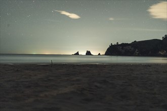 A beach at night with a calm sea atmosphere, starry sky and rocks, Whangamata, New Zealand, Oceania