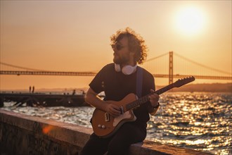 Hipster street rock musician in black playing electric guitar in the street on sunset on embankment