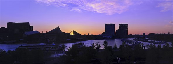 A dramatic and beautiful panoramic sunrise with buildings and boats in silhouette reflected in the