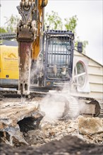 An excavator on a construction site tears down concrete blocks, dust rises, demolition site,