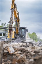 Excavator breaking up concrete on a building site. Debris and dust are scattered around the