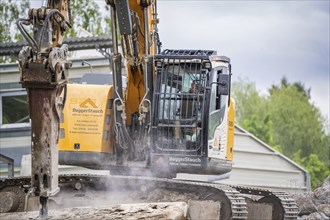 Excavator carrying out demolition work on a building site. A building is visible in the background,