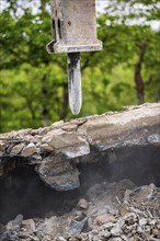 Close-up of the excavator as it breaks up concrete on a construction site. Debris and dust are