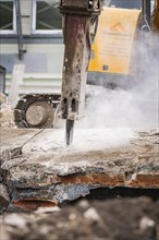 Close-up of an excavator breaking up concrete surrounded by dust and rubble, demolition site,