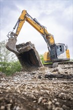 An excavator lifts a large piece of rubble on a building site. The sky is cloudy, demolition site,