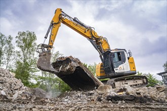 An excavator picks up large pieces of concrete on a construction site, surrounded by rubble and