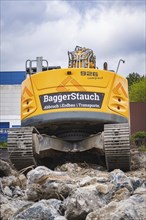 An excavator from behind, surrounded by large rocks on a construction site, the sky is cloudy,