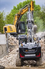 An excavator demolishes a building. Trees and the sky can be seen in the background, demolition