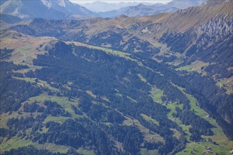 Extensive mountainous landscape with dense forests, green meadows and clear views, Grisons,