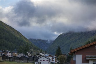 Village in the valley of the Alps with houses surrounded by cloudy mountains under an autumn sky,