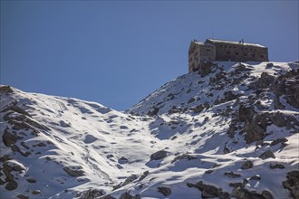 A lonely mountain hut perched on a snow-covered rock, surrounded by a wintry landscape with blue