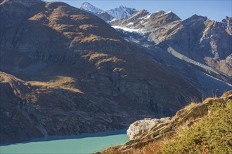 A mountain lake under bright sunlight, surrounded by autumn-coloured mountains and snow-capped