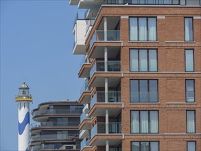 Modern building with balconies and large windows, with a lighthouse in the background, oostende,