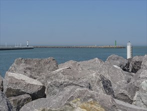 Large rocks on the shore with a lighthouse and a green buoy in the background, oostende, Belgium,