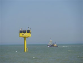 A yellow buoy in the sea with a passing ship under a clear sky, oostende, Belgium, Europe