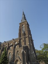 Large Gothic church with high tower and pointed arch windows made of red brick under a clear sky,