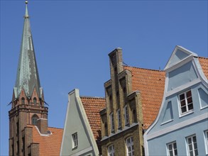 Church tower and historic buildings with colourful facades under a bright blue sky, lüneburg,