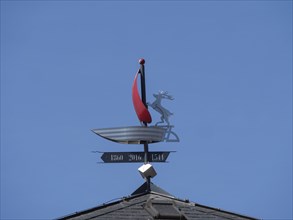 A weather vane in the shape of a boat with a figure under a clear blue sky, lüneburg, germany