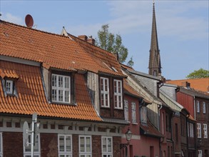 Alley with historic brick houses, red roofs and a church tower in the background under a blue sky,