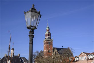 Old lantern with a tower and other buildings in the background under a blue sky, Leer, East Frisia,