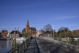 Road leads over a bridge with a view of houses and a tower under a clear sky, Leer, East Frisia,