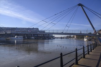 Modern bridge over a river, below floating boats and seagulls, in the background a harbour under a